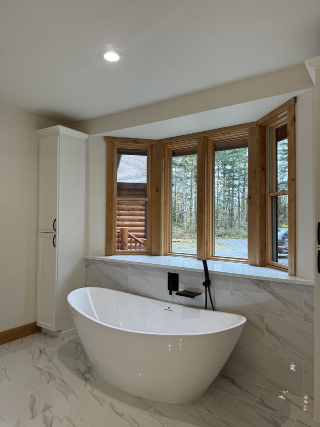 A bathroom with a freestanding tub in front of a bay window