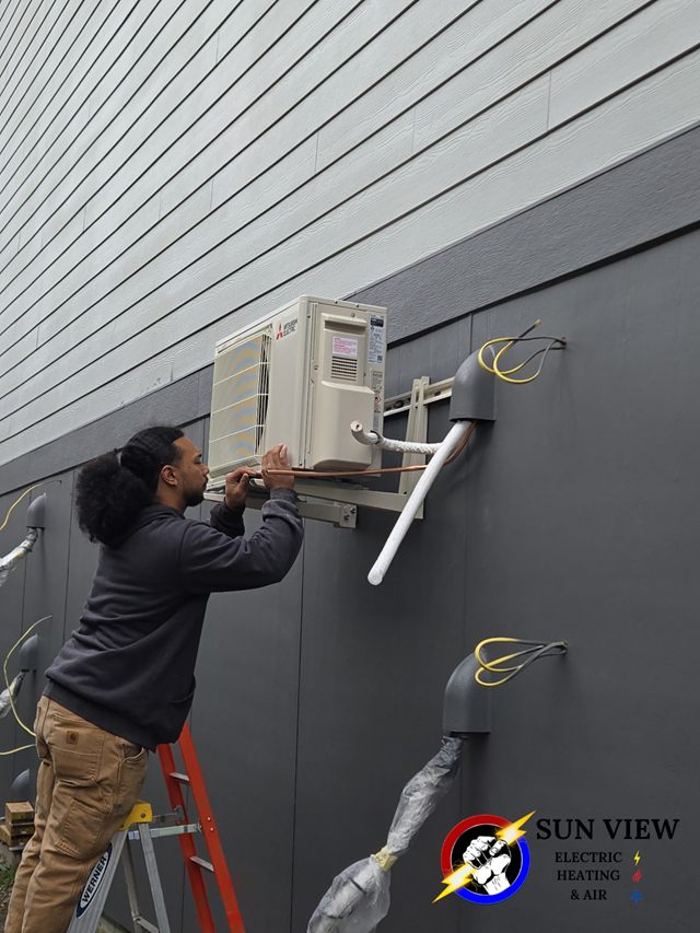 A technician fitting a ductless head to the exterior wall of a house
