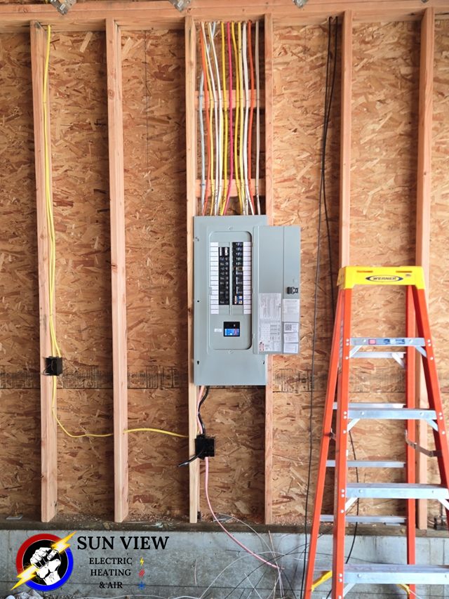 A new electrical panel and conduit runs in a framed wall during rough-in