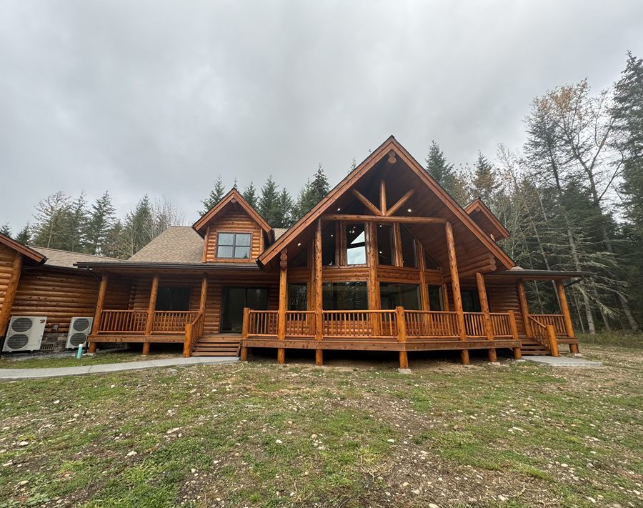 A large log home in the trees with two heat pump condensers visible at the side