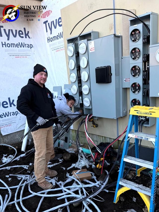A technician wiring a bank of meter bases on a house wrapped for new construction