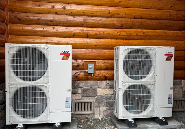 Two Mitsubishi heat pump condensers mounted against the wall of a log home