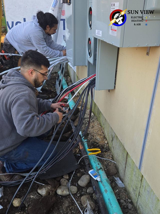 Two Sun View technicians terminating conductors at a new service entrance beside an open trench